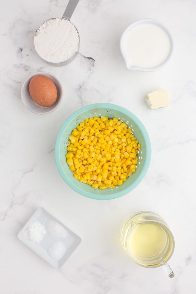 Ingredients for corn nuggets: flour, baking powder, salt, sugar, egg, half and half, butter, canned sweet corn, and canola oil for frying.