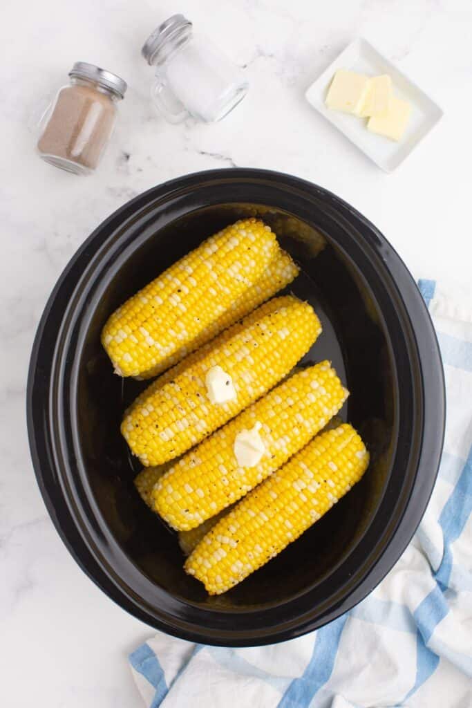 8 ears of corn stacked in two layers in a slow cooker insert.