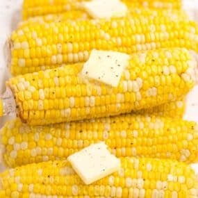 Cooked and buttered ears of corn on a white dinner platter.