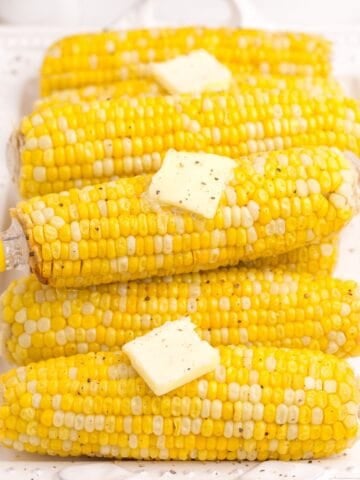 Cooked and buttered ears of corn on a white dinner platter.