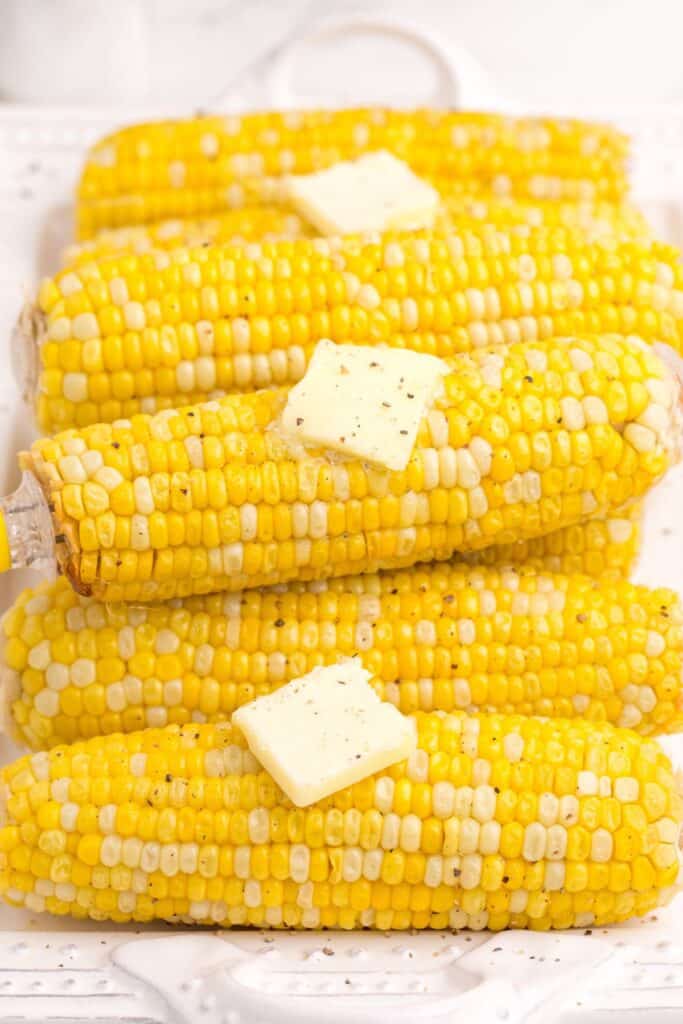 Cooked and buttered ears of corn on a white dinner platter.
