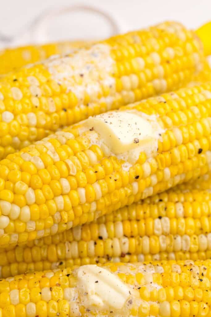 Up close view of corn on the cob piled high with squares on melted butter on them.