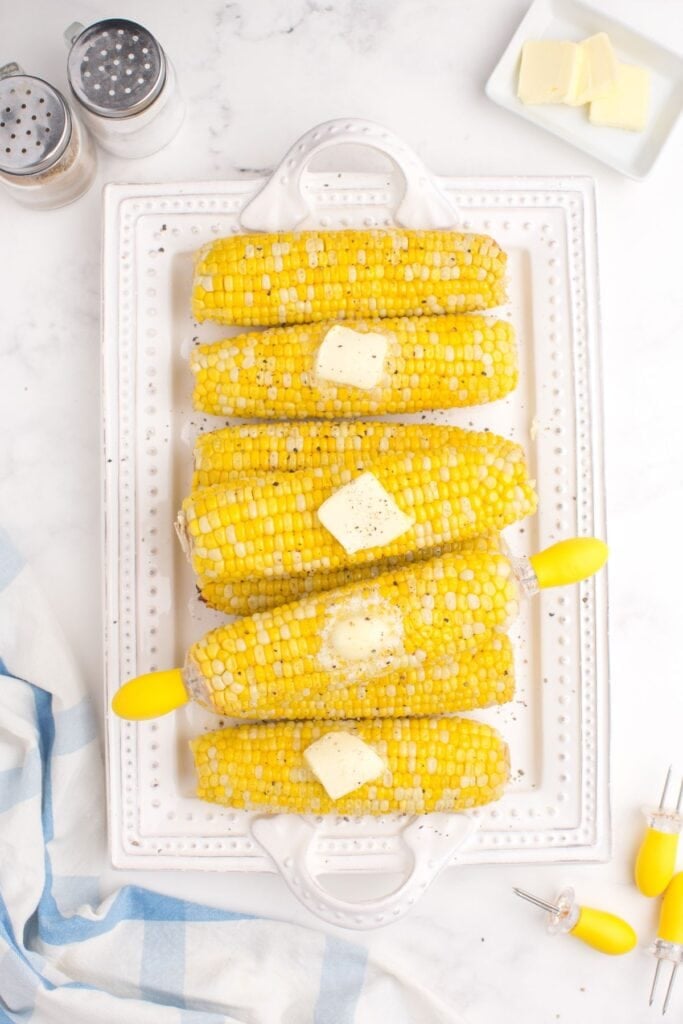 A white serving platter with 8 ears of cooked corn on it.