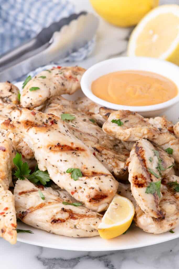 Chicken tenders on a large dinner plate with a dipping sauce in a small bowl.