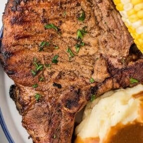 A white and blue dinner plate with a large pork chop on it.