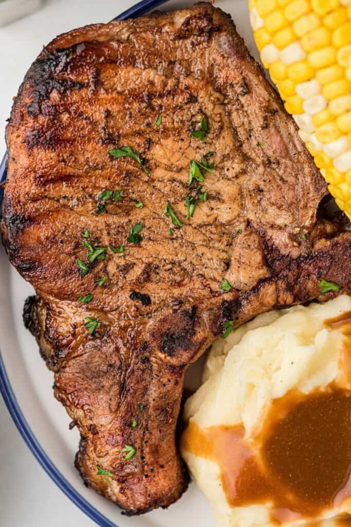 A white and blue dinner plate with a large pork chop on it.
