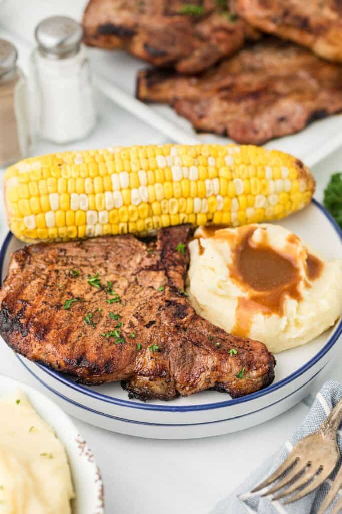 White and blue dinner plate with a large grilled pork chop, mashed potatoes with gravy, and corn on the cob.