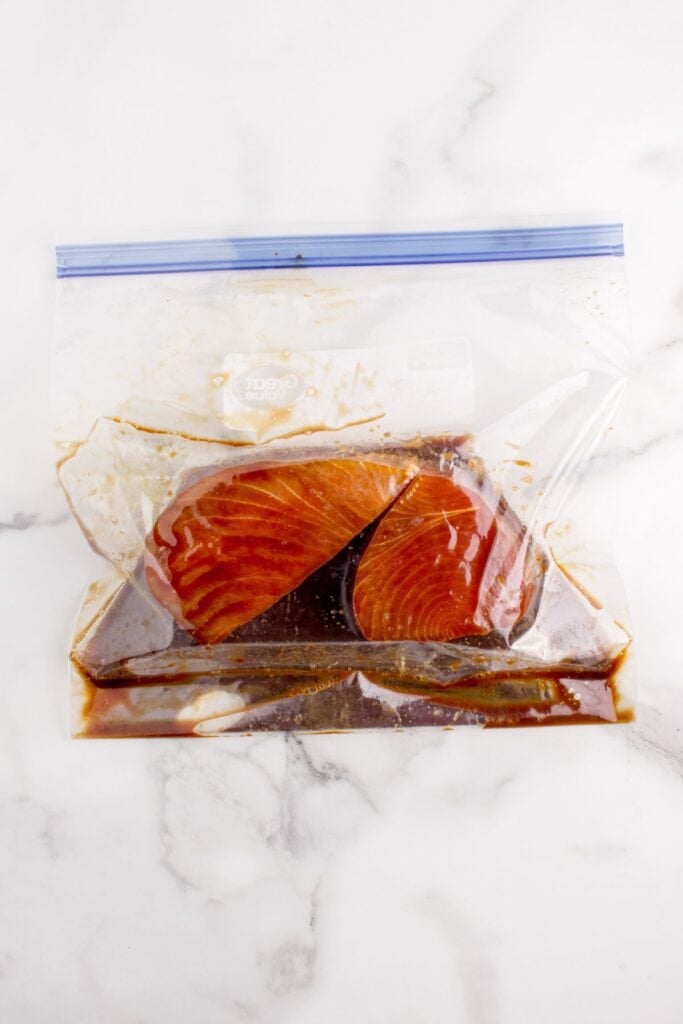 A zip top bag with two tuna steaks in a marinade.