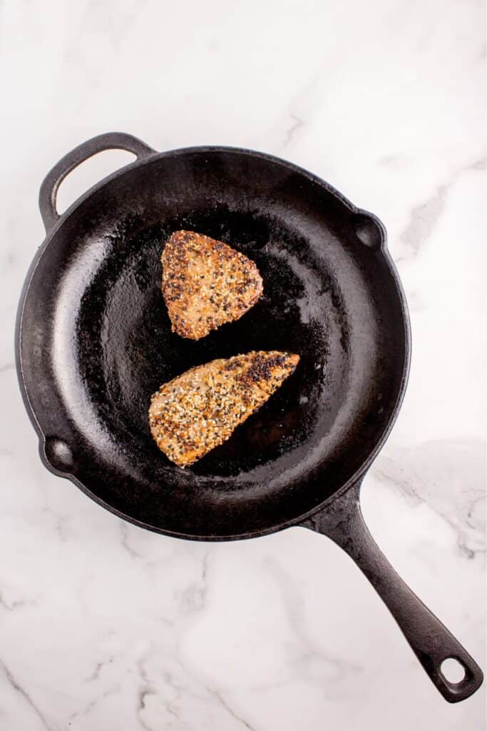 Tuna steak cooking in a cast iron pan.