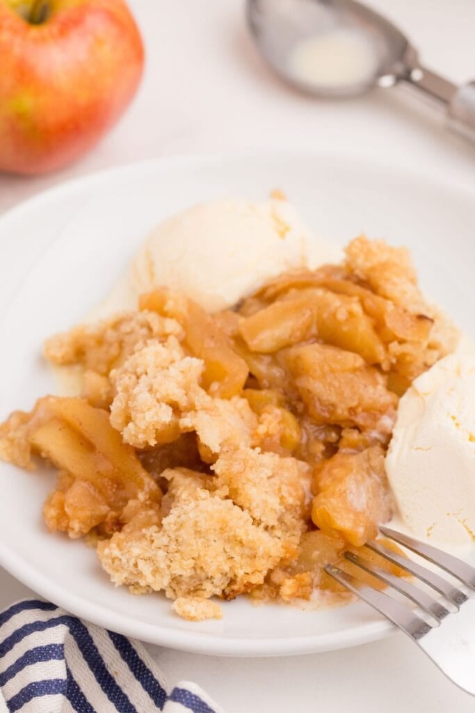 Apple crisp in a white bowl with two scoops of ice cream and a fork.