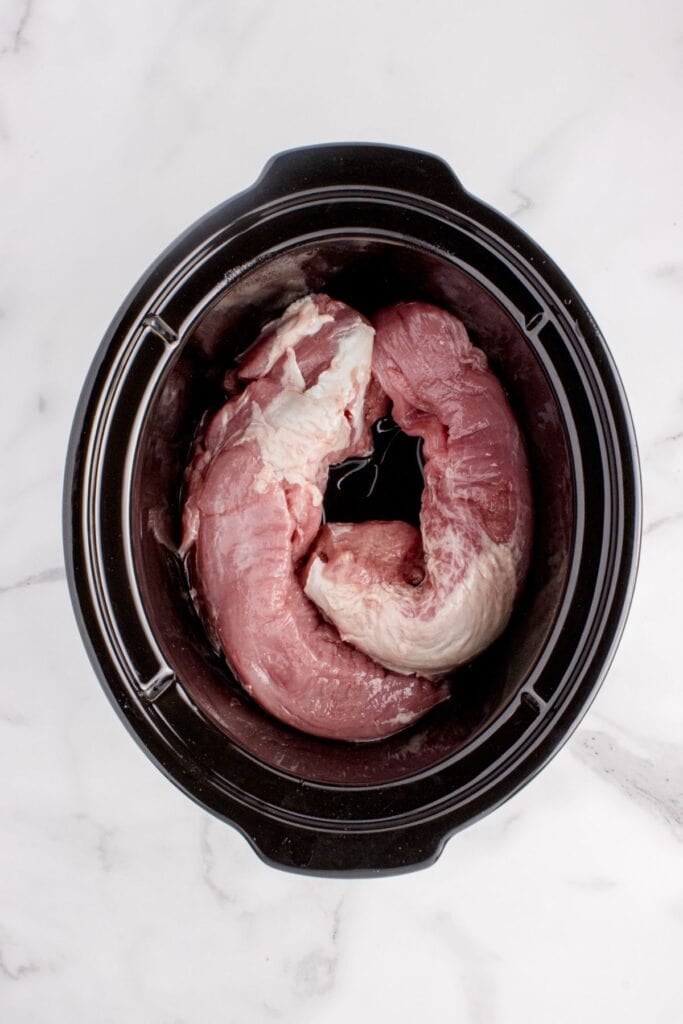 Raw pork tenderloin in a crock pot insert.