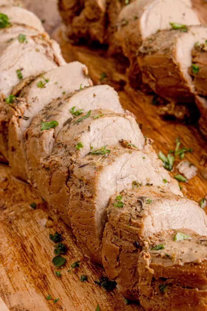 Sliced pork tenderloin on a wooden cutting board. Close up image to show interior or pork tenderloin.