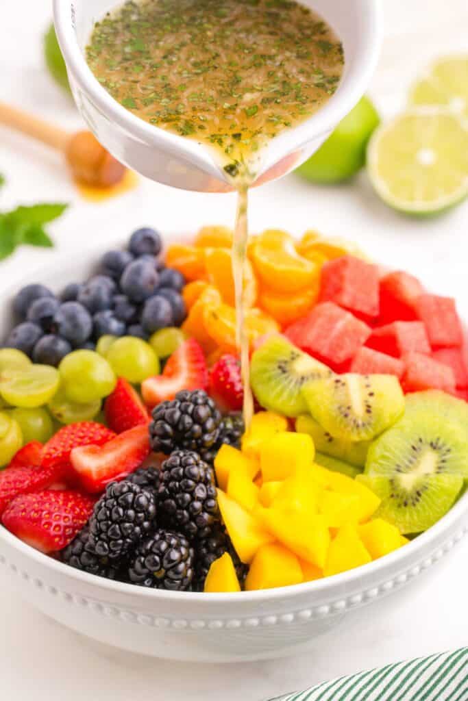 Close up of fruit salad dressing being poured over fresh fruit.