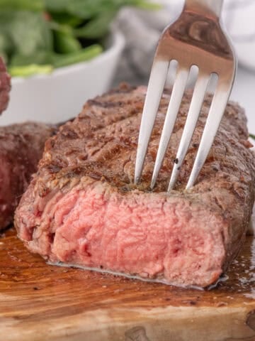 A fork is piercing the grilled sirloin steak.