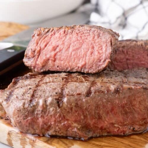 Two steaks stacked on top of each other. The top steak is sliced in half to show the interior.