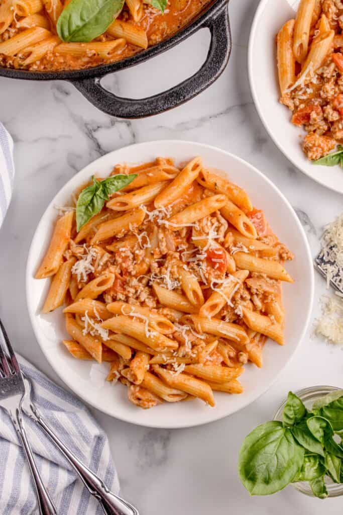 Pasta recipe served on a white dinner plate with grated parmesan and a sprig of basil for garnish.