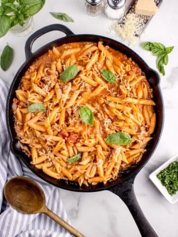 Ground turkey pasta in a black cast iron pan garnished with grated parmesan and basil leaves.