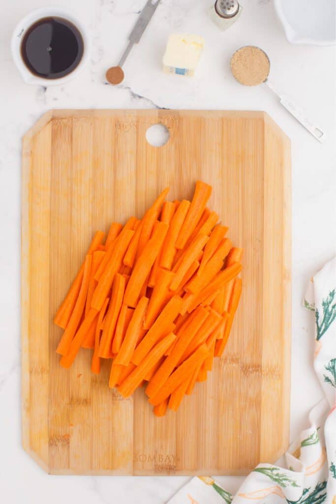 Peeled and chopped carrots on a wooden cutting board. Ingredients for the maple glaze are arranged above the cutting board.