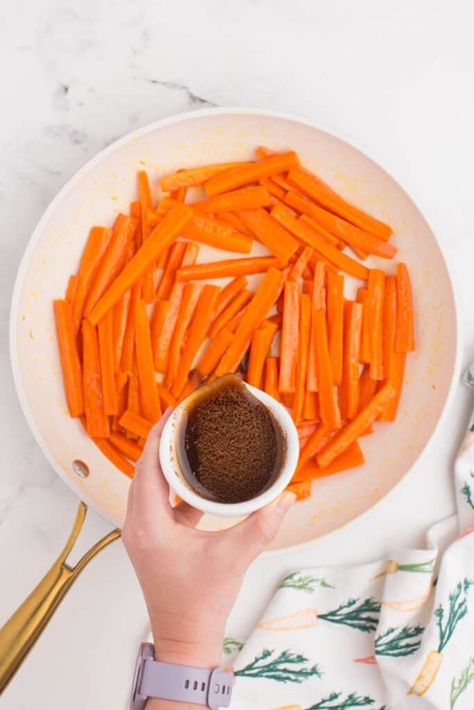 Maple glaze ingredients being poured over the carrots in a skillet.