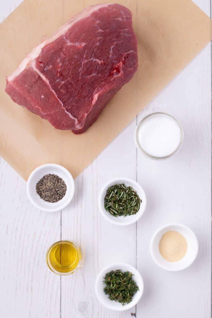 Ingredients for bottom round roast: bottom round roast, salt, olive oil, fresh rosemary, fresh thyme leaves, black pepper, and garlic powder.
