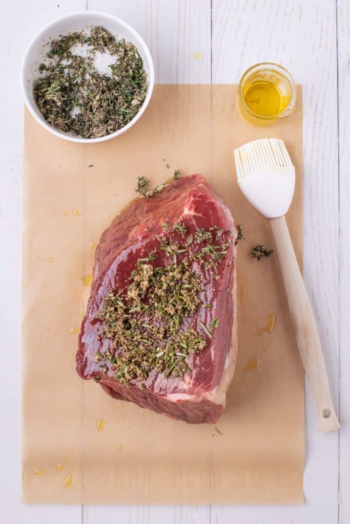 The roast has been basted with oil and sprinkled with seasoning on a piece of parchment paper.