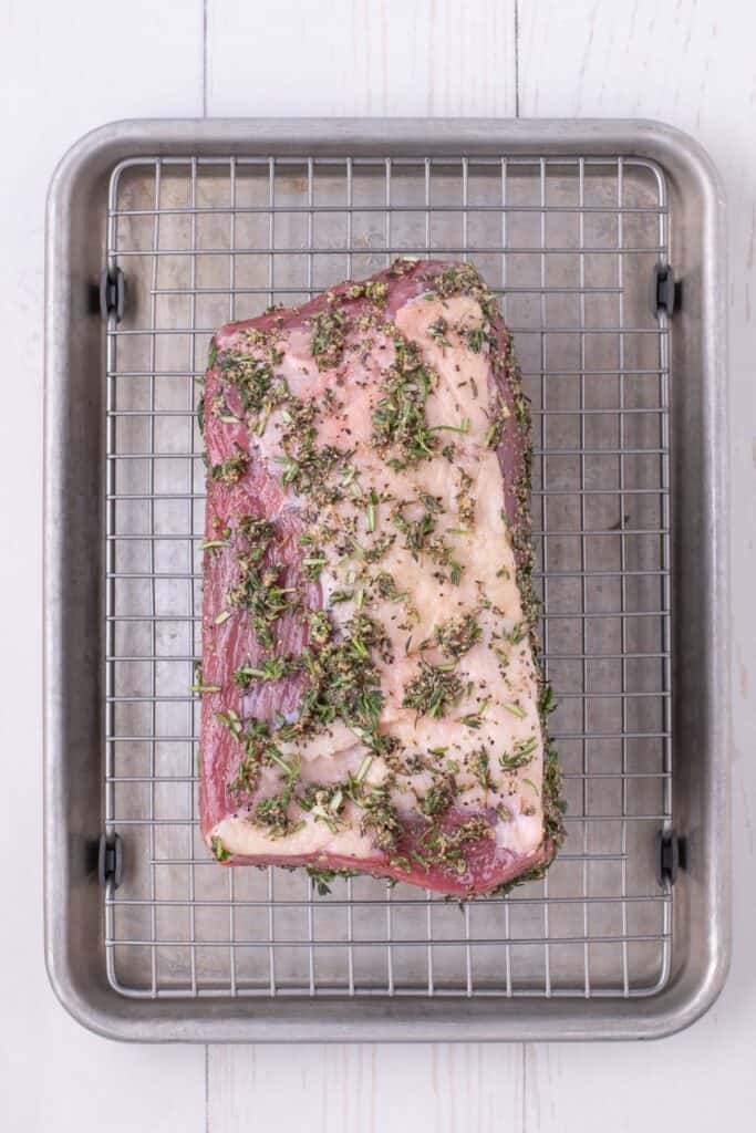 Uncooked, seasoned roast placed on a wire rack over a sheet pan.