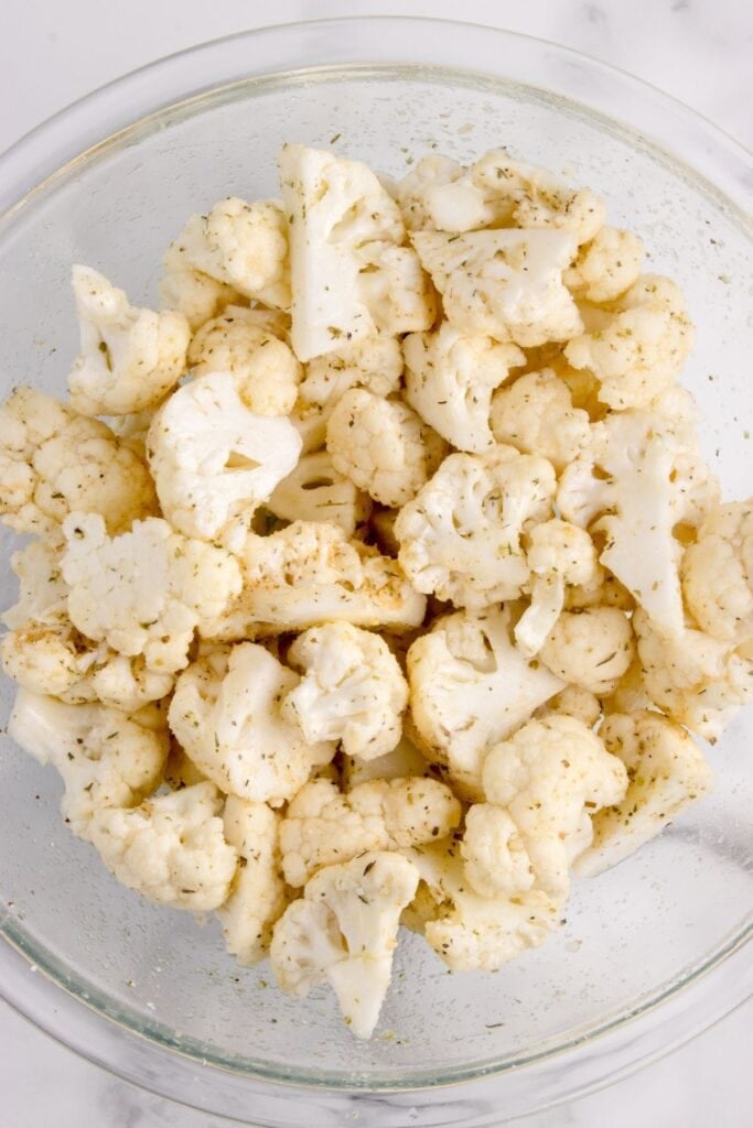 A glass bowl with seasoned raw cauliflower in it.