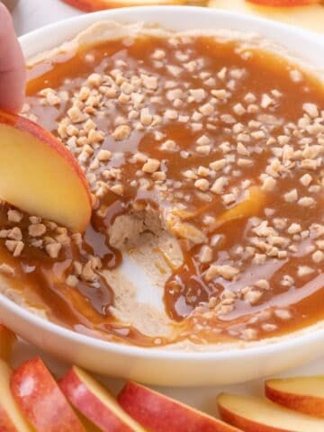 An apple is scooping up a bite of caramel dip.