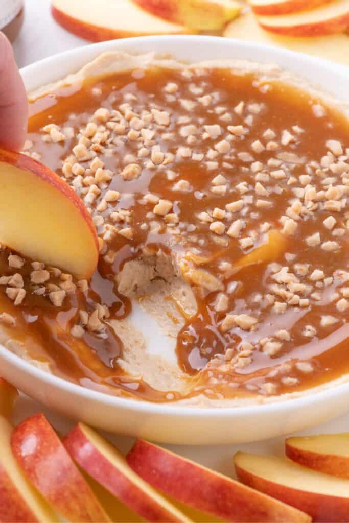 An apple is scooping up a bite of caramel dip.