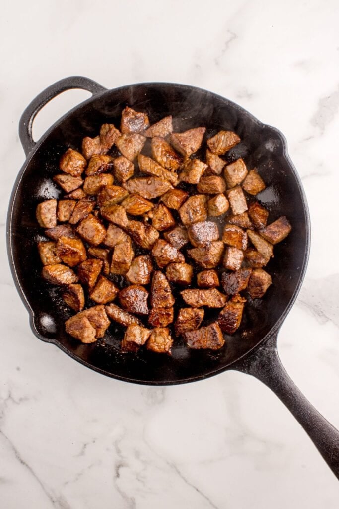 Steak bites cooking in a cast iron pan.