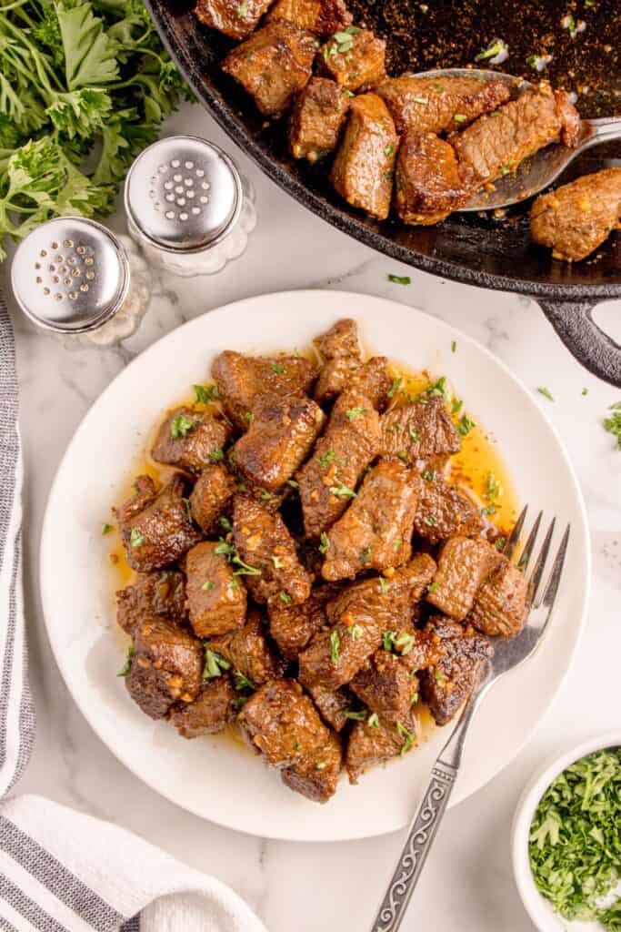 Garlic butter steak bites piled high on a white dinner plate.