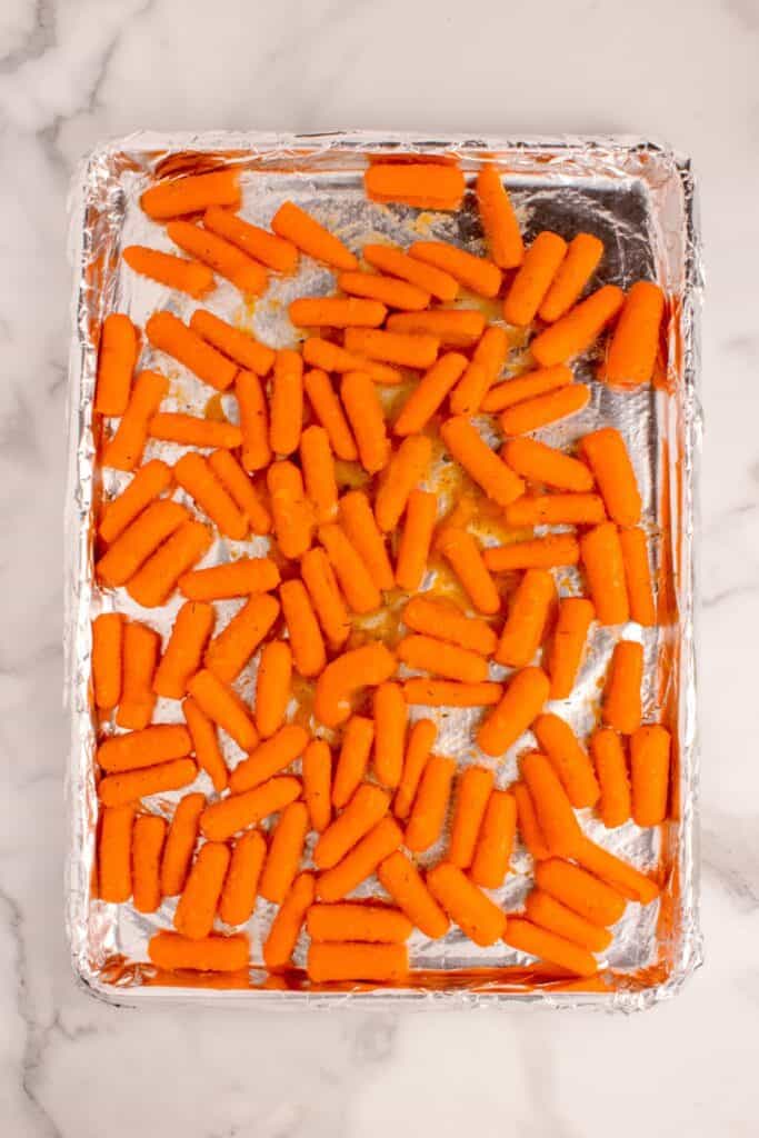 Raw seasoned carrots on an aluminum foil lined baking sheet.