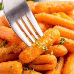 A fork is piercing a roasted baby carrot.