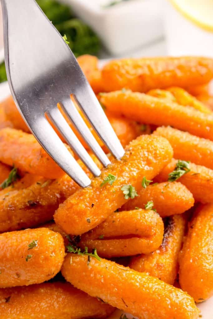 A fork is piercing a roasted baby carrot.