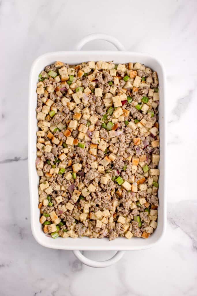 Uncooked sausage stuffing in a white baking dish.