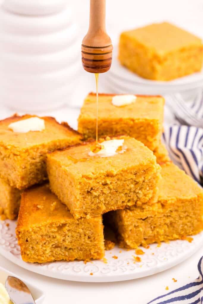 Honey being drizzled over a stack of sliced cornbread.