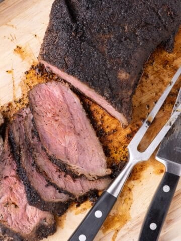 Large tri tip partially sliced and fanned out on a wooden cutting board.