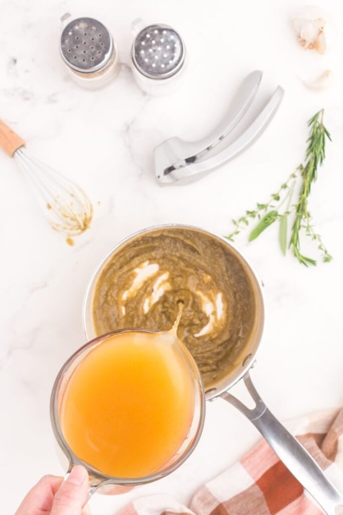 Turkey broth being poured into a saucepan with a thickened slurry of herbs, spices, butter, and flour.