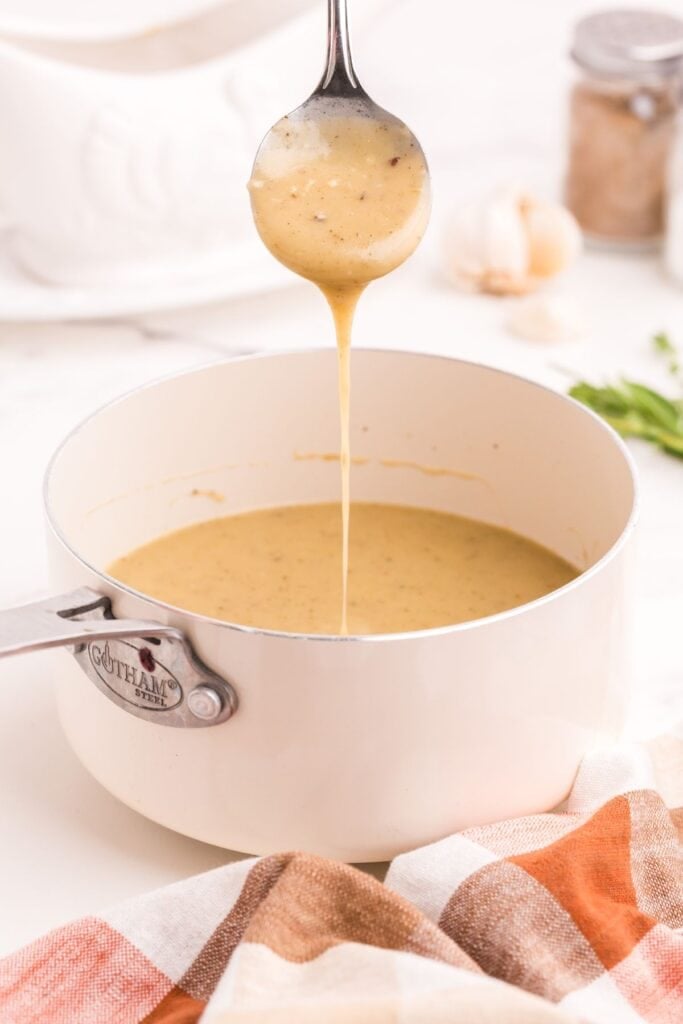 A saucepan with completed turkey gravy in it. A spoon is drizzling gravy back into the saucepan to show the thickness.