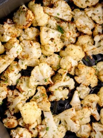 Close up of crispy cauliflower in an air fryer basket.
