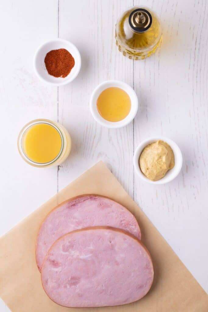 Ingredients for ham steaks: olive oil, honey, orange juice, Dijon mustard, cayenne pepper, and boneless ham steaks.