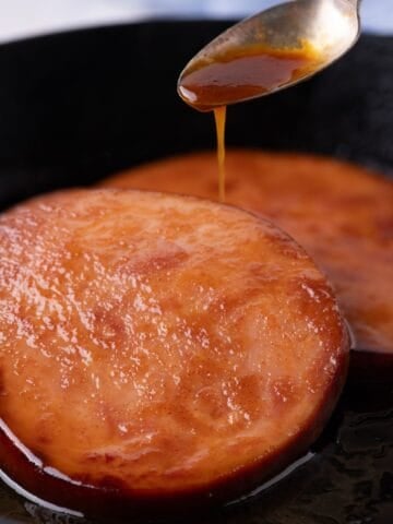 Two ham steaks in a cast iron pan being drizzled with glaze.
