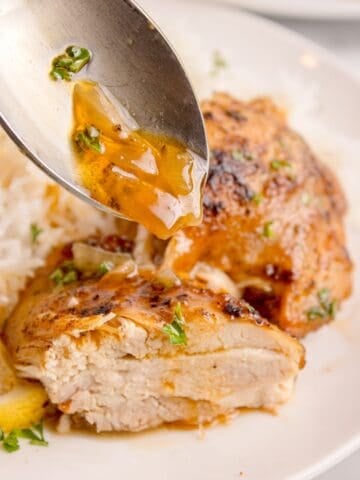 Cooked chicken thighs with a spoon drizzling an onion gravy on top.