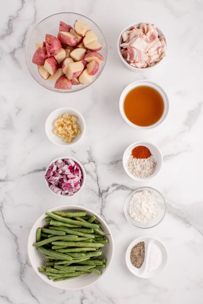 Ingredients for smothered green beans: thick-cut bacon, red onion, minced garlic, flour, onion soup mix powder, smoked paprika, chicken broth, fresh green beans, red potatoes, salt, and black pepper.