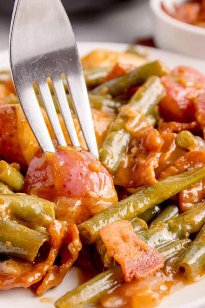 A fork piercing a potato in the smothered green beans recipe.