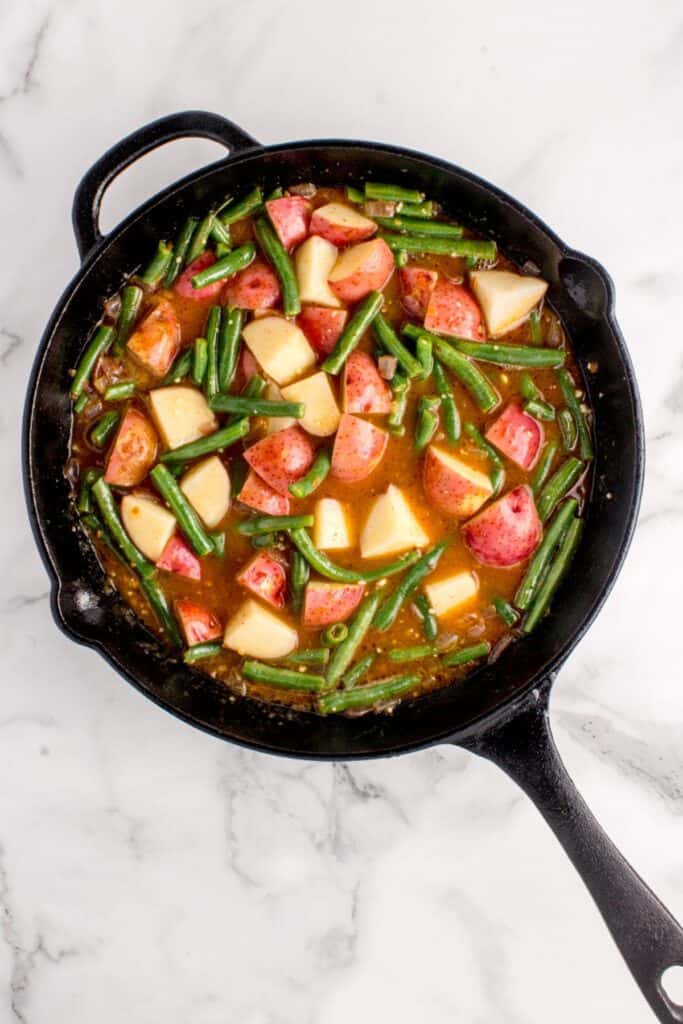 Green beans and potatoes added to bacon, onion, and broth mixture.