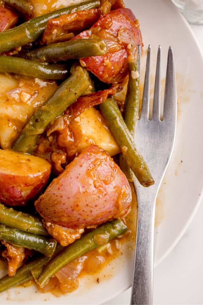 Smothered green beans recipe on a white dinner plate with a fork.