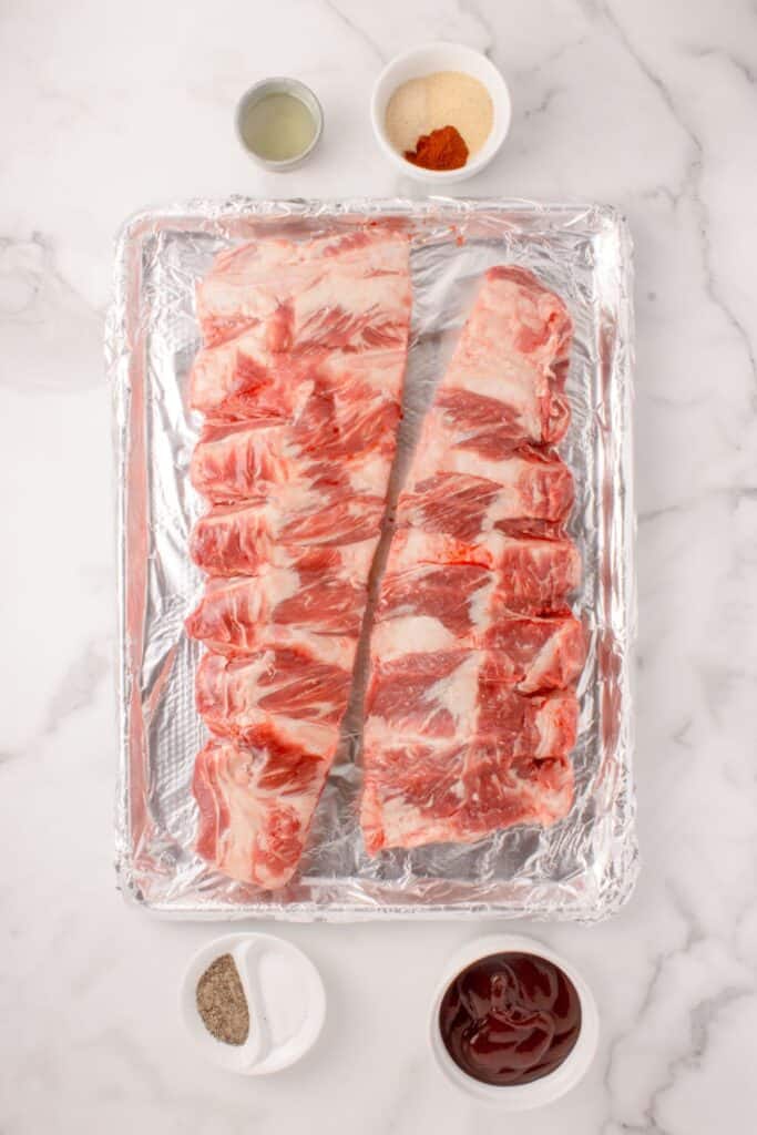 Ingredients for beef ribs in the oven: beef back ribs, olive oil, salt, black pepper, garlic powder, onion powder, smoked paprika, and barbecue sauce.