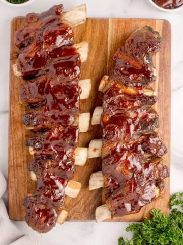 Two racks of finished beef ribs on a wooden cutting board.