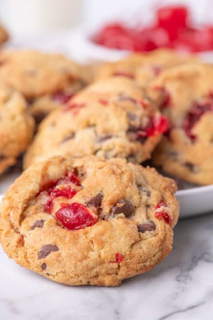 A white serving platter with cherry cookies lined up on it. A single cookie is propped up on the edge of the plate to show detail.